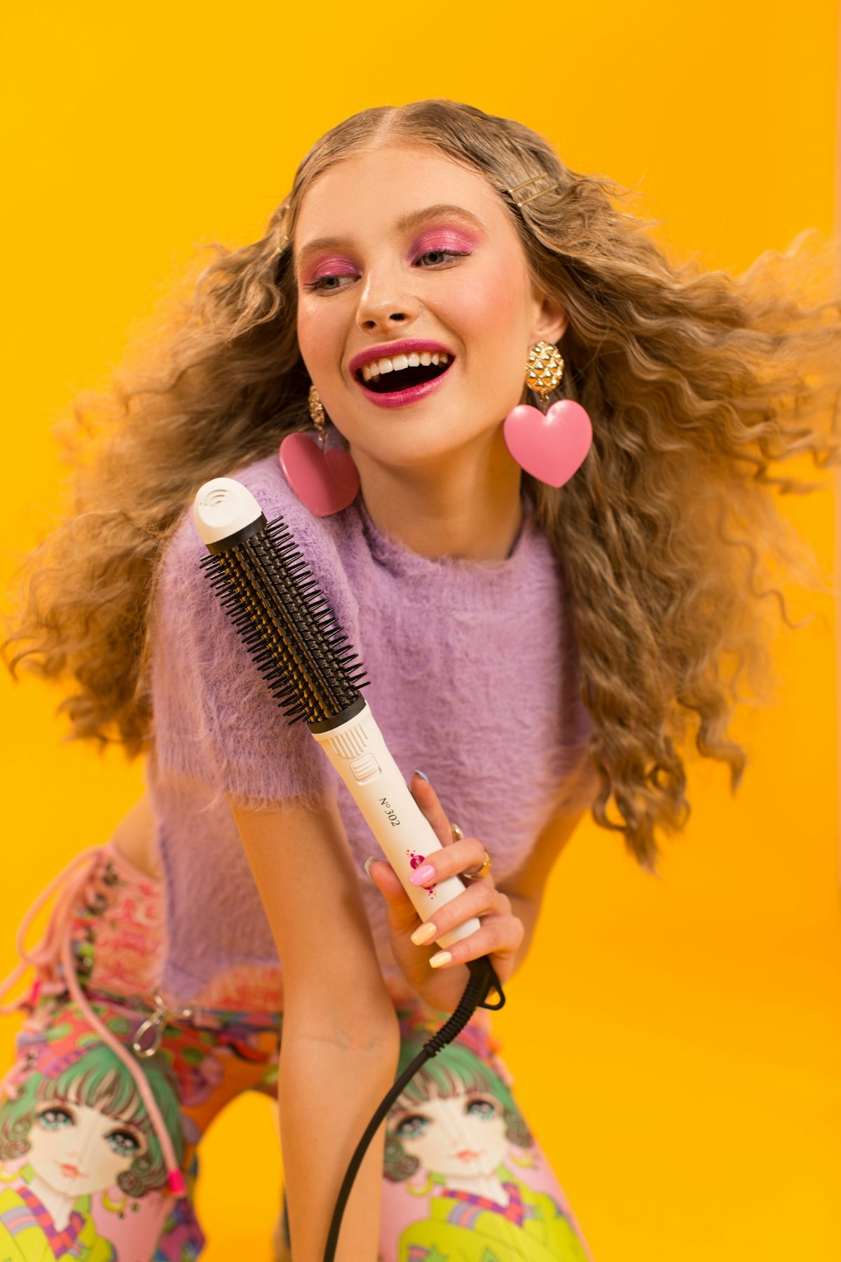 Smiling woman with curly hair holding a hair styling tool.
