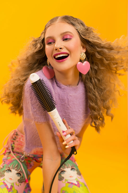 Smiling woman with curly hair holding a hair styling tool.