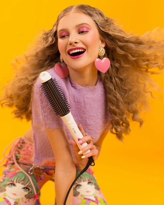 Smiling woman with curly hair holding hairbrush on yellow background.